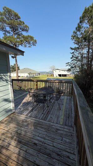 A wooden deck with a table and chairs, surrounded by a wooden railing, overlooking a residential area with houses and trees.