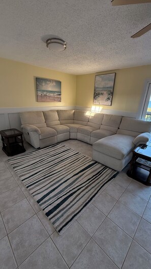 A living room with a beige sectional sofa, a striped rug, and two wall-mounted paintings.