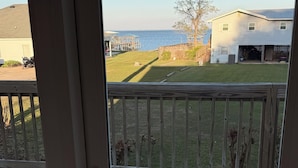 A view from a sliding glass door onto a wooden deck with a grassy yard and a house in the background. - Stunning Mobile Bay views near Dauphin Island (Coden)