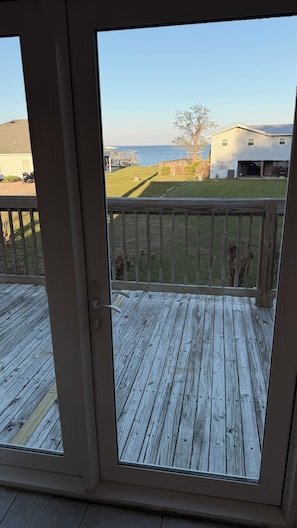 A view from a sliding glass door onto a wooden deck with a grassy yard and a house in the background.