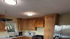 A kitchen with wooden cabinets, a marble island, stainless steel appliances, and a hanging pot rack. - Stunning Mobile Bay views near Dauphin Island (Coden)