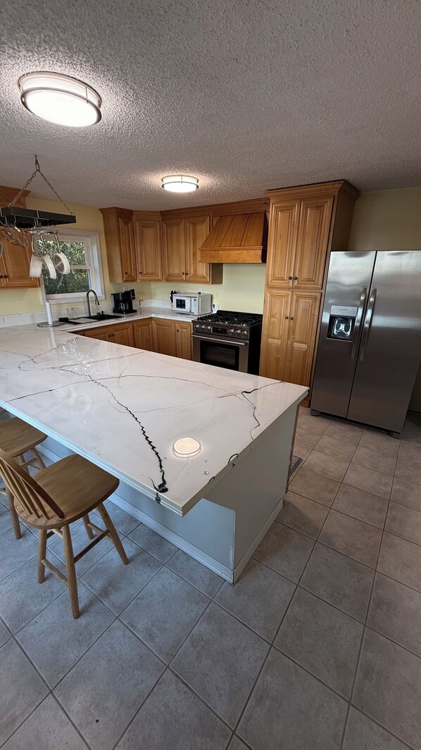 A kitchen with wooden cabinets, a marble island, stainless steel appliances, and a hanging pot rack.
