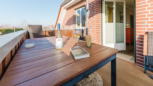 Eine Holzterrasse mit Tisch, einer Weinflasche, einem Glas und einem Buch.
