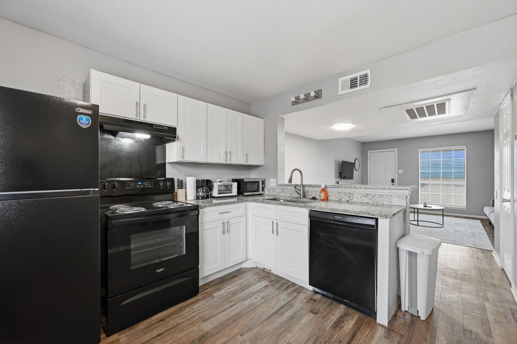 A modern kitchen with white cabinets, a black refrigerator, a stove, a microwave, and a dishwasher.