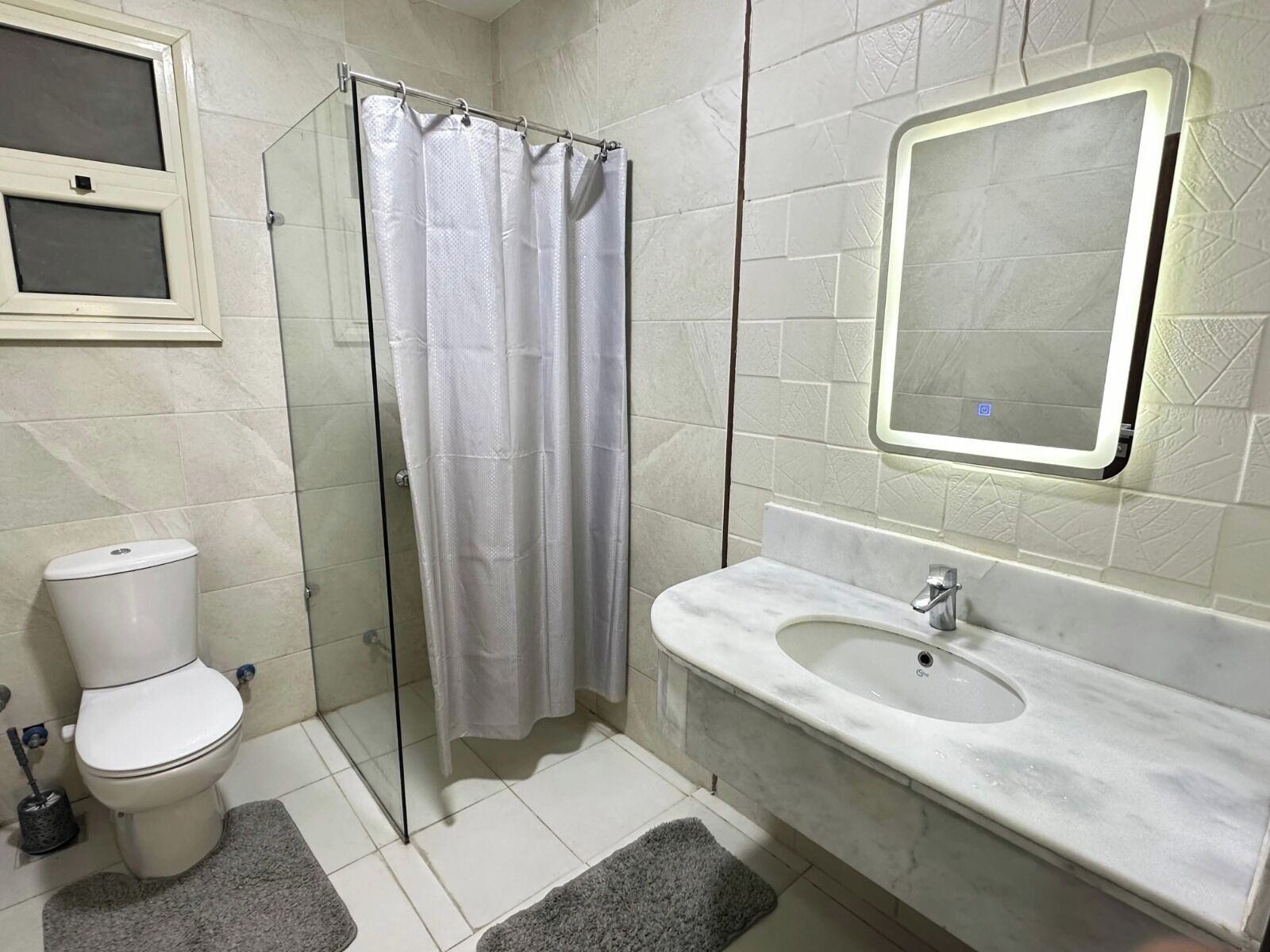 A bathroom with a toilet, a glass shower enclosure, a sink, and a mirror.