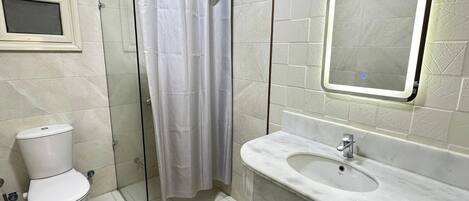 A bathroom with a toilet, a glass shower enclosure, a sink, and a mirror.