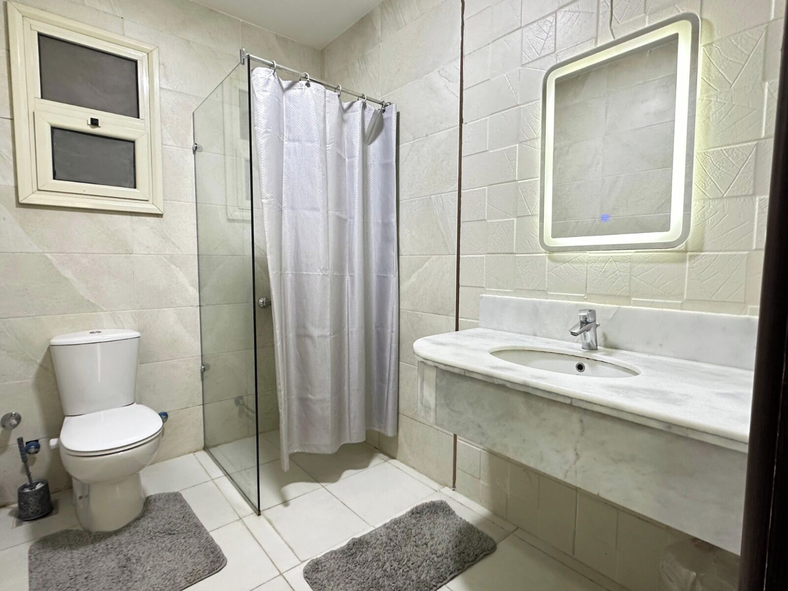 A bathroom with a toilet, shower, sink, and mirror.