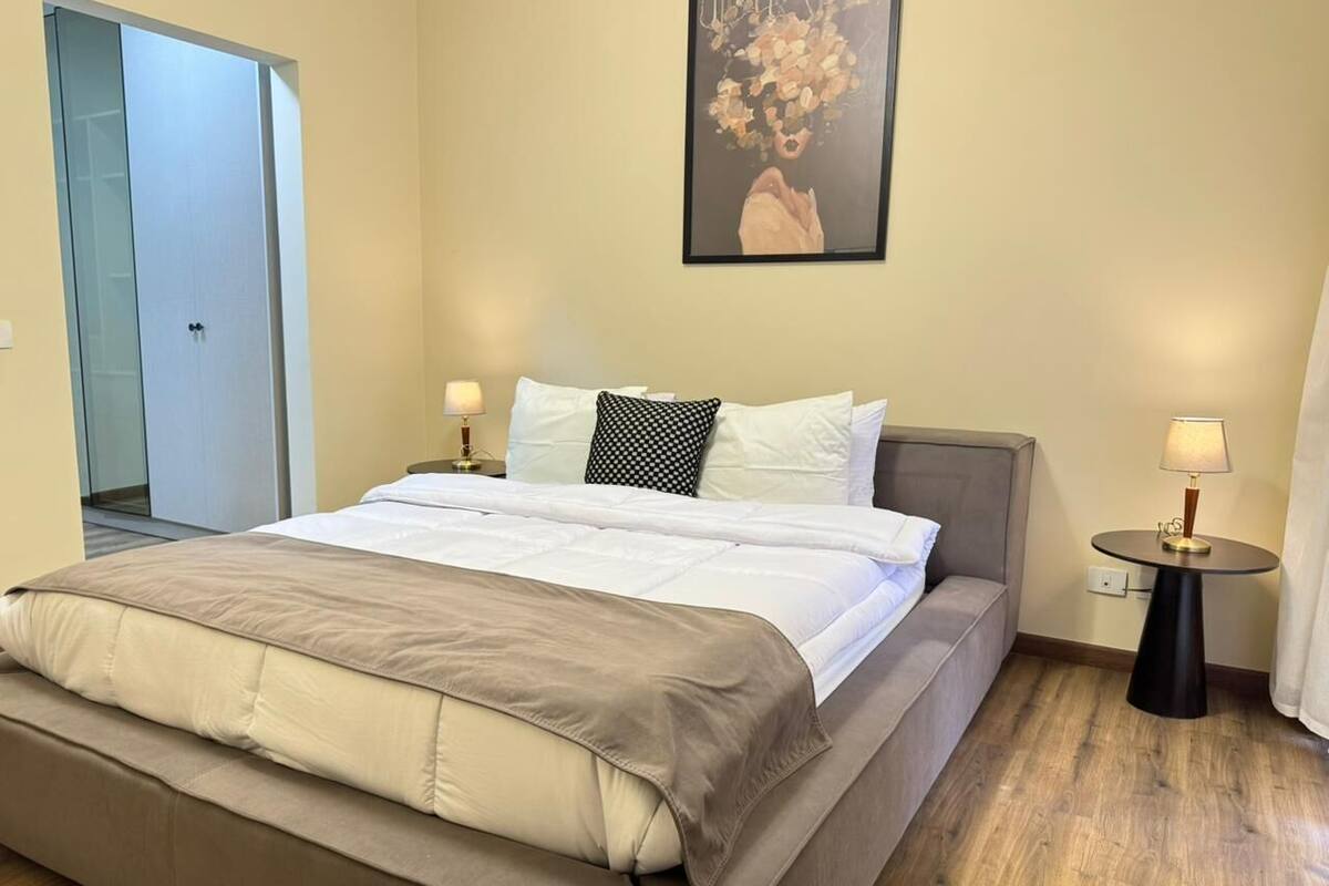 A bedroom with a bed, bedside tables, a door, and a painting on the wall.
