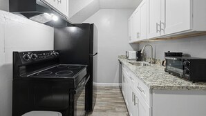 Una cocina compacta con armarios blancos, una estufa negra, un microondas y un tostador.