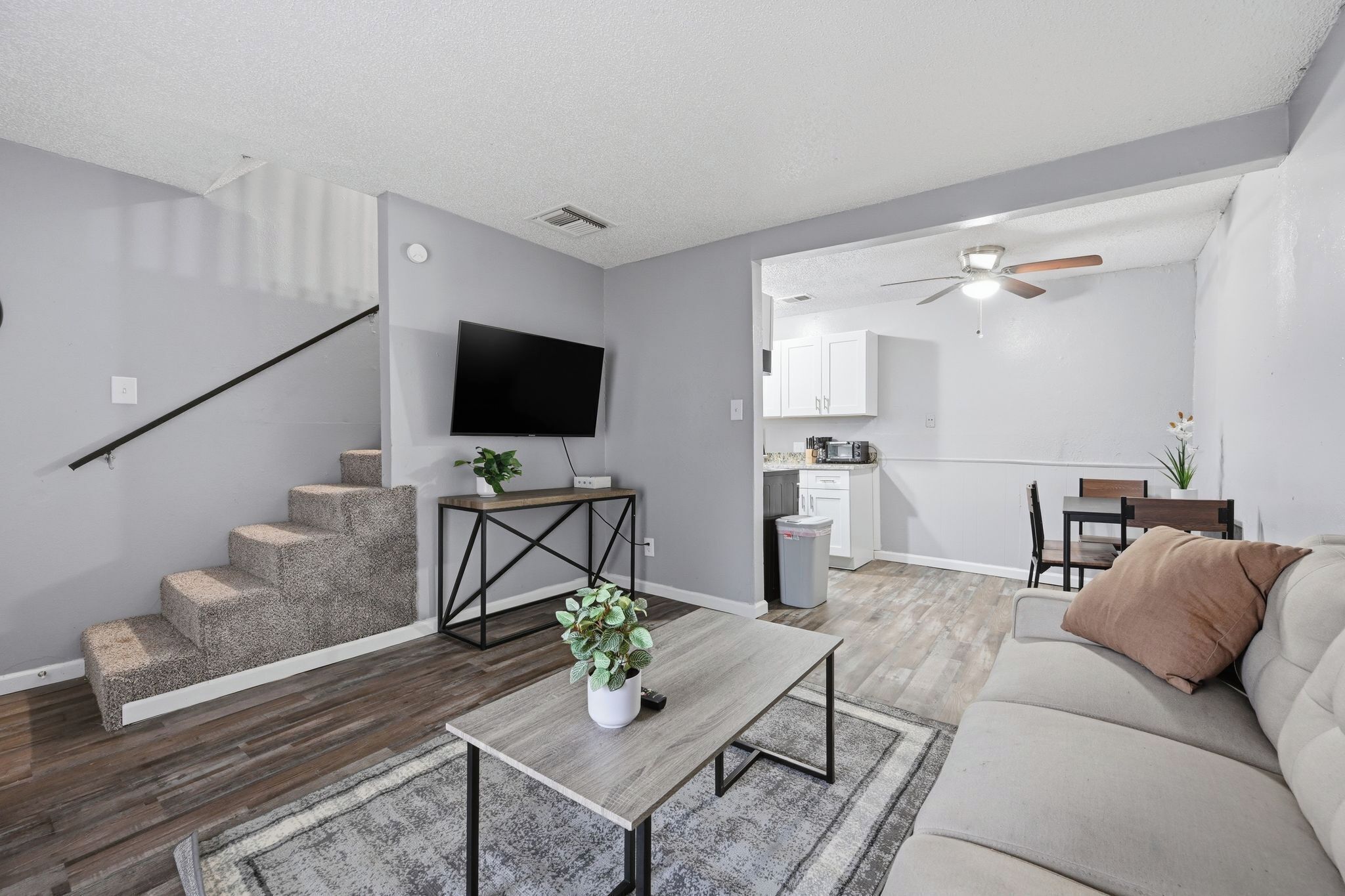 A living room with a staircase, a flat-screen TV, a dining area, and a kitchen in the background.