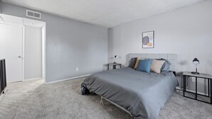 Un dormitorio con cama, mesitas de noche, cabecero, una puerta y un cuadro colgado en la pared.