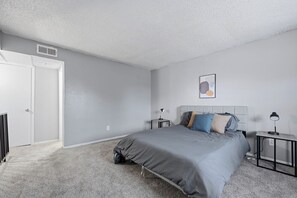 A bedroom with a bed, bedside tables, a headboard, a door, and a wall-mounted picture. - Roomy 1BR townhome with open living area (Arlington)