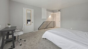 Quarto com cama, escrivaninha, cadeira, um vaso pequeno com planta, porta branca e escada.