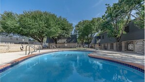 Piscina com borda azulejada, cercada por árvores e um cercado.