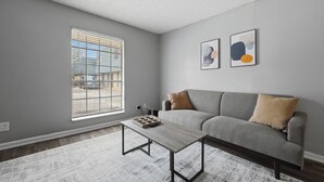 A living room with a gray sofa, a coffee table, and two abstract paintings on the wall. - Comfortable 1BR townhome with full kitchen (Arlington)