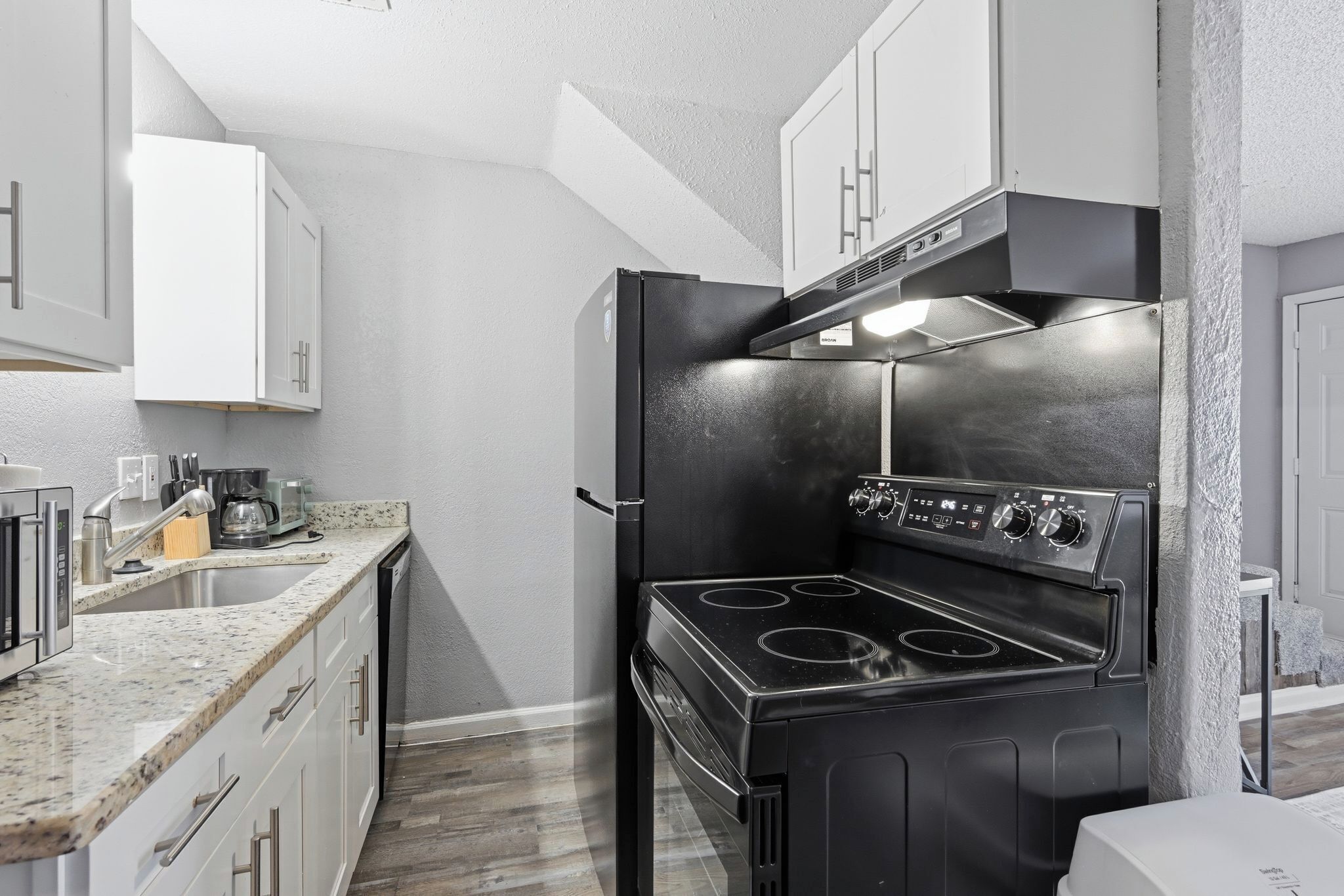 A compact kitchen with white cabinets, a black stove, and a sink.