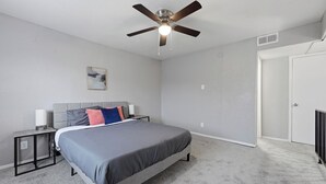 A bedroom with a bed, a nightstand, a ceiling fan, a wall-mounted lamp, and a door. - Comfortable 1BR townhome with full kitchen (Arlington)