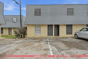 A building with a fire lane marked on the ground, a parking area, and a vehicle parked in front. - Comfortable 1BR townhome with full kitchen (Arlington)