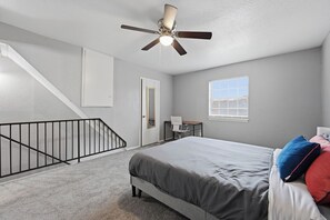 A bedroom with a bed, a ceiling fan, a window, a door, and a staircase. - Comfortable 1BR townhome with full kitchen (Arlington)