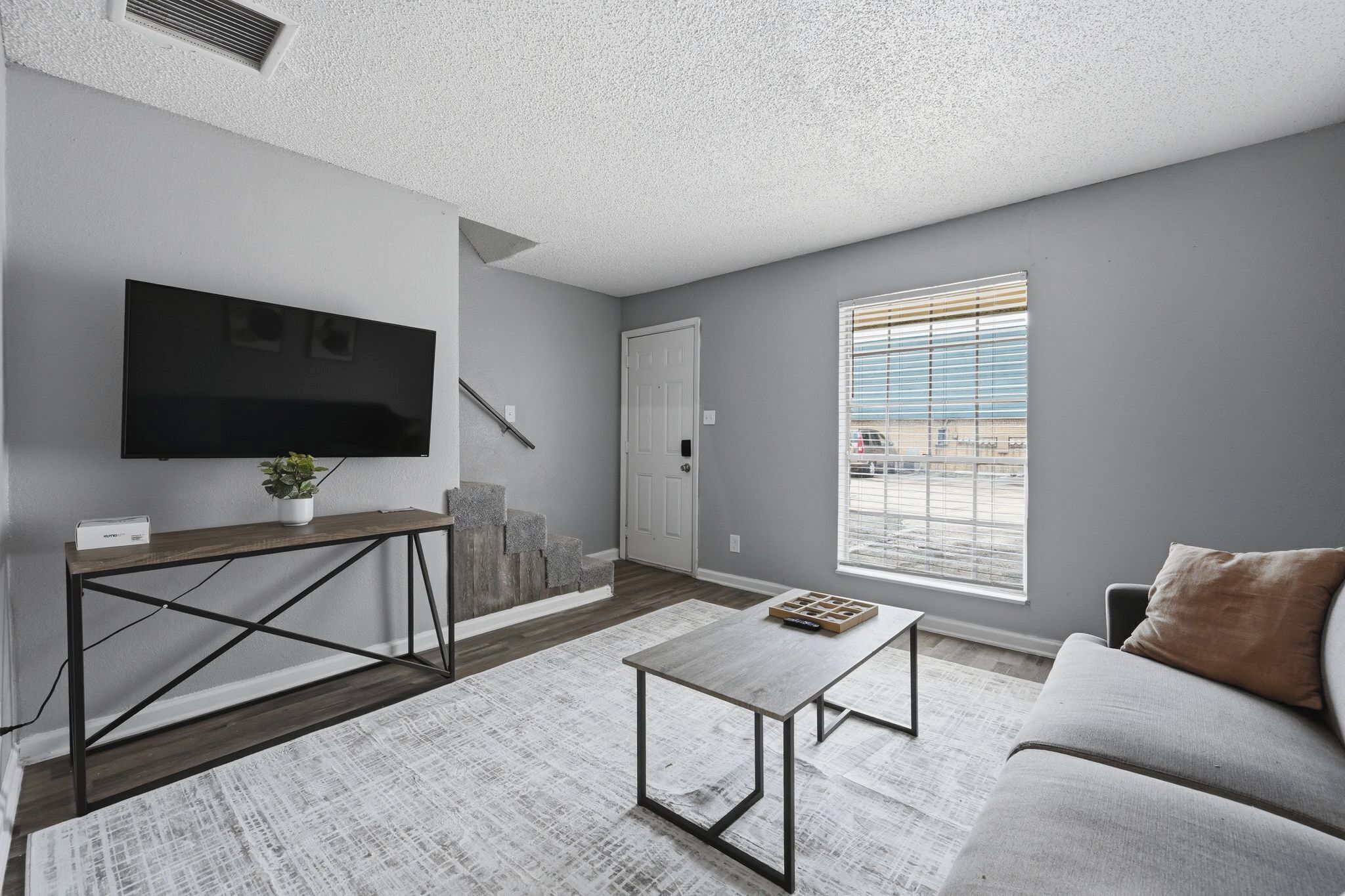 A living room with a TV, a coffee table, a sofa, a staircase, and a window with blinds.