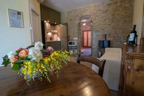 A dining area with a wooden table, a bouquet of flowers, a stone wall, and a television in the background. - Nice room for 4 guests with A/C, pool, WIFI, TV, veranda and pets allowed, close to Perugia (Agello)