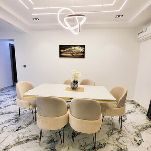 A modern dining area with a white table, beige chairs, a vase of flowers, and a painting on the wall. - Lofty Xphere Apartment (Abuja)
