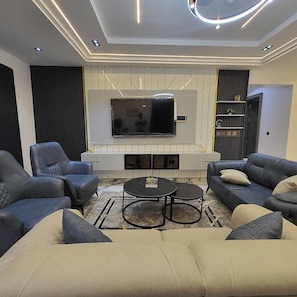 A modern living room with a large flat-screen TV, two sofas, a coffee table, and a fireplace. - Lofty Xphere Apartment (Abuja)