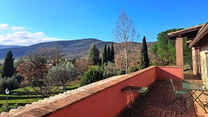 Un balcón con vistas a un paisaje montañoso, una pared de ladrillo y una mesa de metal con sillas.