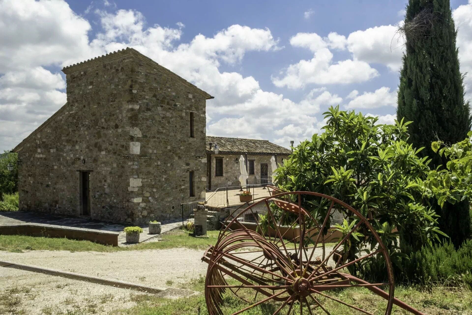 A stone building with a flat roof, a small porch, and a large metal wheel structure.