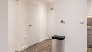 A hallway with white walls, a trash bin, and a door. - Round The Clock Bookings - Wharf 1ne (Barking)