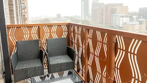 A balcony with wicker furniture and a patterned railing, overlooking a cityscape. - Round The Clock Bookings - Wharf 1ne (Barking)