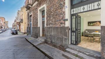 Straßenansicht eines Gebäudes mit steinverkleideter Fassade, einem verschlossenen Eingang und einem durch das Fenster einsehbaren Essbereich.
