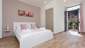 A bedroom with a large bed, a painting on the wall, a door leading to an outdoor area, and a small table with chairs. - 'Vitali Home' - Apartment in the Heart of Catania (Catania)