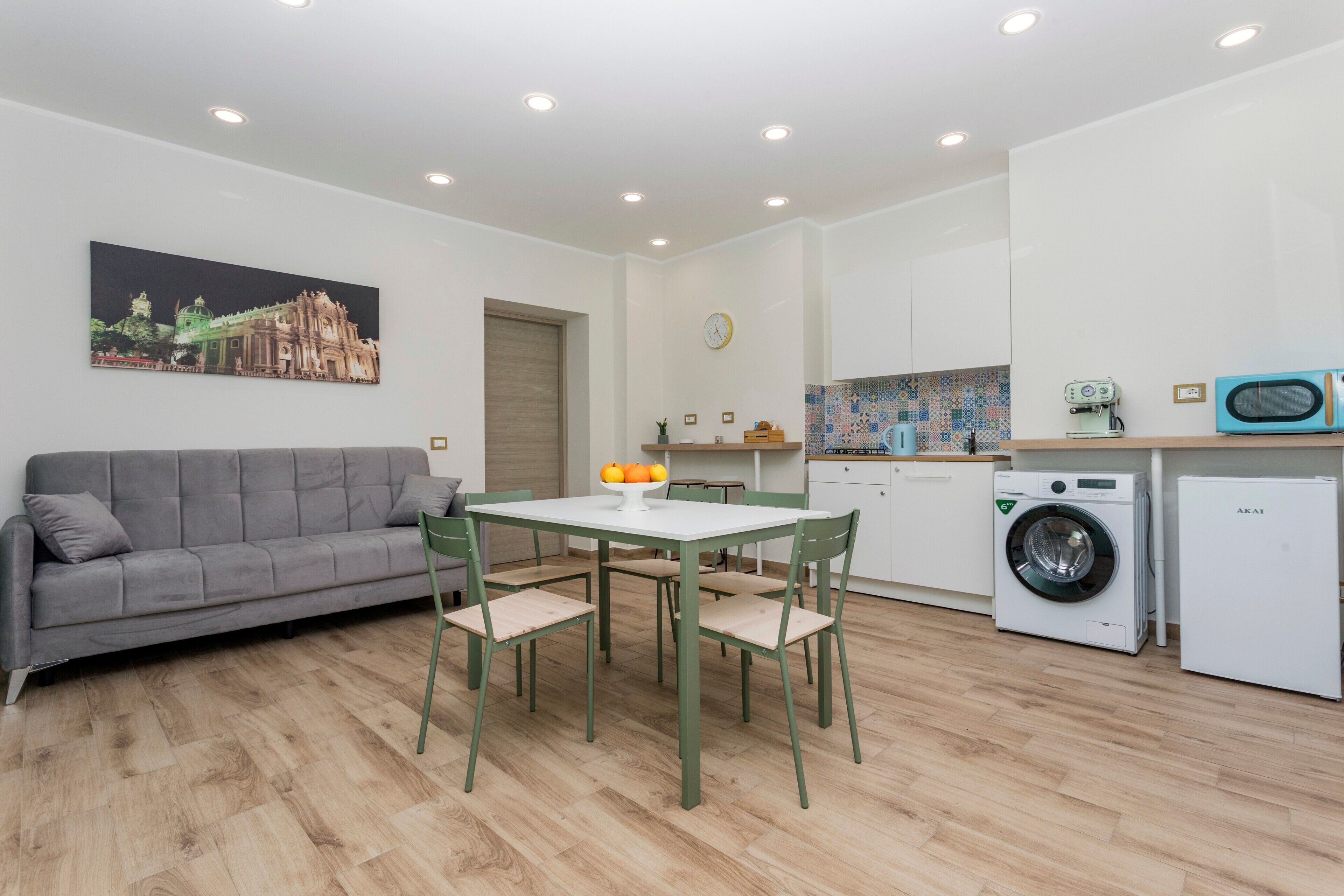 Ein kompakter Wohnraum mit Sofa, Esstisch, Stühlen, einer Waschmaschine und einer Mikrowelle.