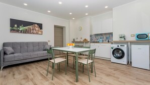A compact living space with a sofa, dining table, chairs, a washing machine, and a microwave. - 'Vitali Home' - Apartment in the Heart of Catania (Catania)