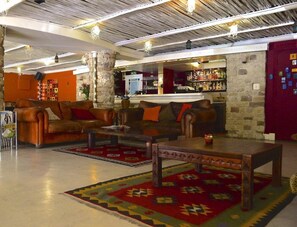 Un hall con sofás de cuero, una mesa de centro, un tapete estampado, un pilar de piedra y una zona de bar con botellas.