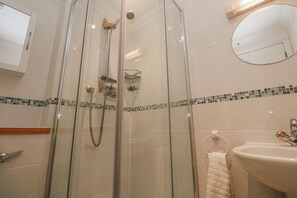 A glass-enclosed shower with a handheld showerhead, a wall-mounted mirror, and a sink with a towel rack. - Seaside Retreat (St Ives)