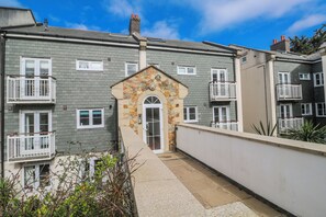 A multi-story residential building with a stone facade, white railings, and a central entrance with a door. - Seaside Retreat (St Ives)