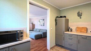 Eine kompakte Küche mit Mikrowelle, Toaster und Kaffeemaschine. Im angrenzenden Wohnbereich befindet sich ein graues Sofa.