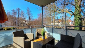 Ein Balkon mit Korbmöbeln, einem Tisch und einem Blumentopf.