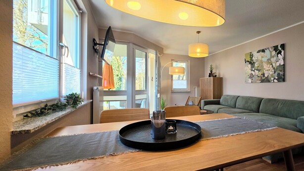 Ein modernes Wohnzimmer mit einem Holzesstisch, einem grünen Sofa und einem großen Fenster mit Jalousien.