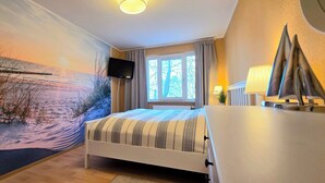 Ein Schlafzimmer mit einem Bett, einem Fernseher, einem Fenster mit Vorhängen und Wandbild.