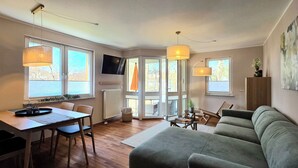Ein Wohnzimmer mit einer Couch, einem Esstisch mit Stühlen, einem an der Wand befestigten Fernseher und einem großen Fenster mit Blick.