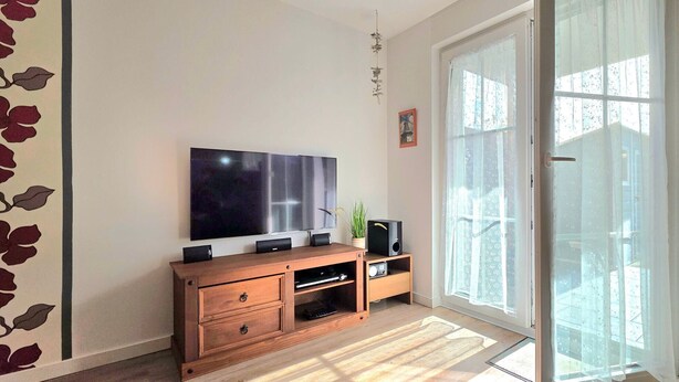 Sala de estar con televisor de pantalla plana, mueble bajo de madera, puerta corrediza de vidrio y una pequeña planta.