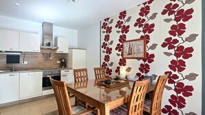 Una cocina moderna con armarios blancos, microondas, estufa y un comedor con mesa y sillas de madera.