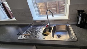 Une cuisine équipée d’un évier en acier inoxydable, d’un égouttoir, d’une bouteille de liquide vaisselle et d’une bouilloire.