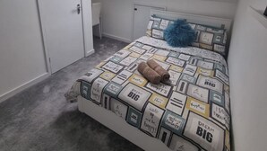 Une chambre avec un puits de lumière, un lit recouvert d’une courtepointe à motifs, un oreiller bleu et un ours en peluche.
