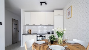 A modern kitchen with white cabinets, a wooden dining table with placemats, and a vase with flowers. - Apartamenty Sun & Snow Miodowa (Warsaw)