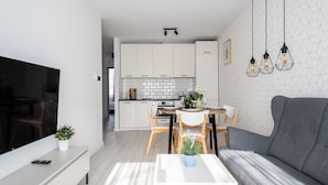 A modern living room with a flat-screen TV, a grey sofa, a white coffee table, and a dining area with wooden chairs and a white table. - Apartamenty Sun & Snow Miodowa (Warsaw)