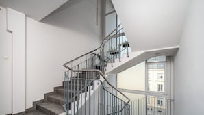 A modern staircase with metal railings, a tiled floor, and a view of buildings outside through large windows. - Apartamenty Sun & Snow Miodowa (Warsaw)